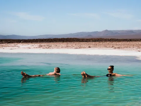Atacama tours combo, twee bezoekers drijven in een turquoise zoutlagune met woestijnbergen erachter