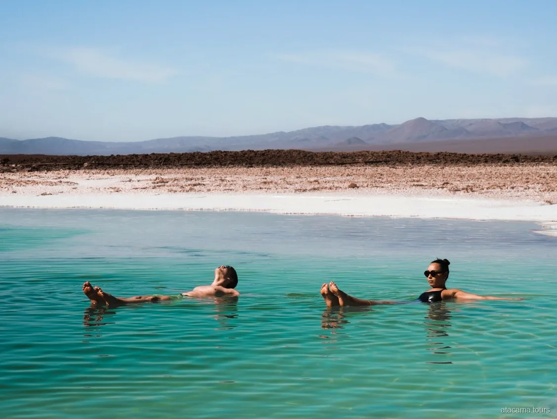 Atacama tours combo, twee bezoekers drijven in een turquoise zoutlagune met woestijnbergen erachter