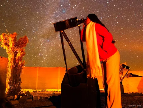 Atacama tours combo, traveler looking through a large telescope under a starry desert sky at night