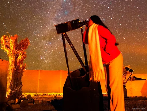 Passeios no Atacama, viajante olhando por um grande telescópio sob o céu estrelado do deserto à noite