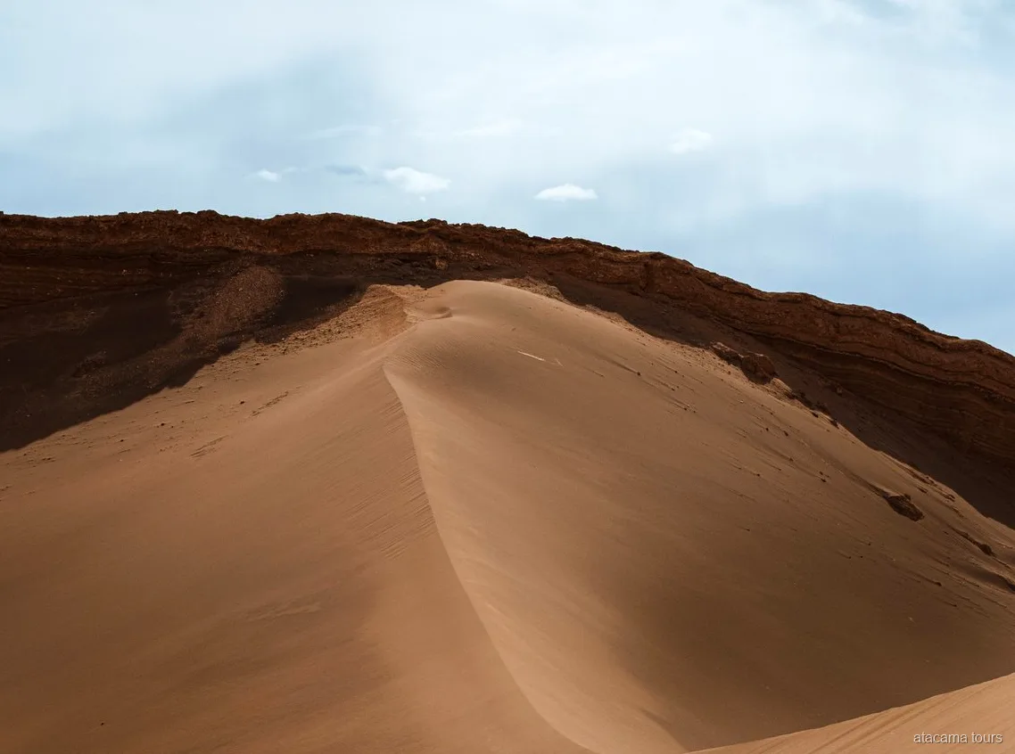 Passeios no Atacama pelo Valle de la Luna, duna de areia lisa curvando sob uma crista de rocha escura