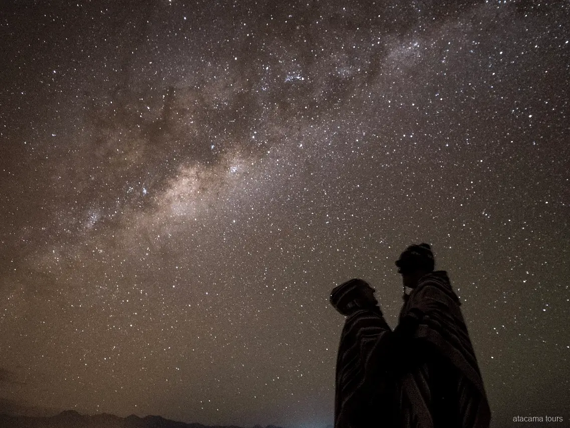 Atacama stargazing tours, twee silhouetten in poncho's onder een dichte band van de Melkweg
