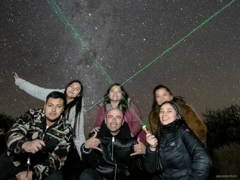 Passeios astronômicos no Atacama, grupo sorridente posando sob o céu noturno com lasers verdes