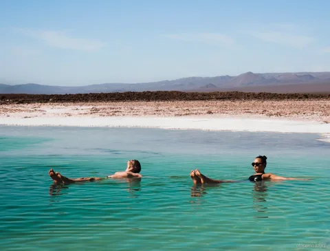 Tour ad Atacama, due visitatori che galleggiano in una laguna salata turchese con montagne sullo sfondo