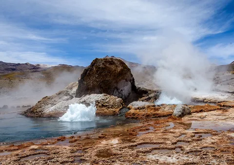 Passeios no Atacama a El Tatio, gêiser borbulhando ao lado de uma grande rocha com vapor e minerais