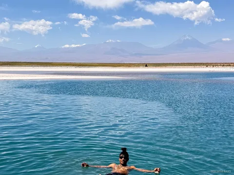 Passeios no Atacama à Laguna Cejar, banhista flutuando na água azul com vulcões nevados ao fundo