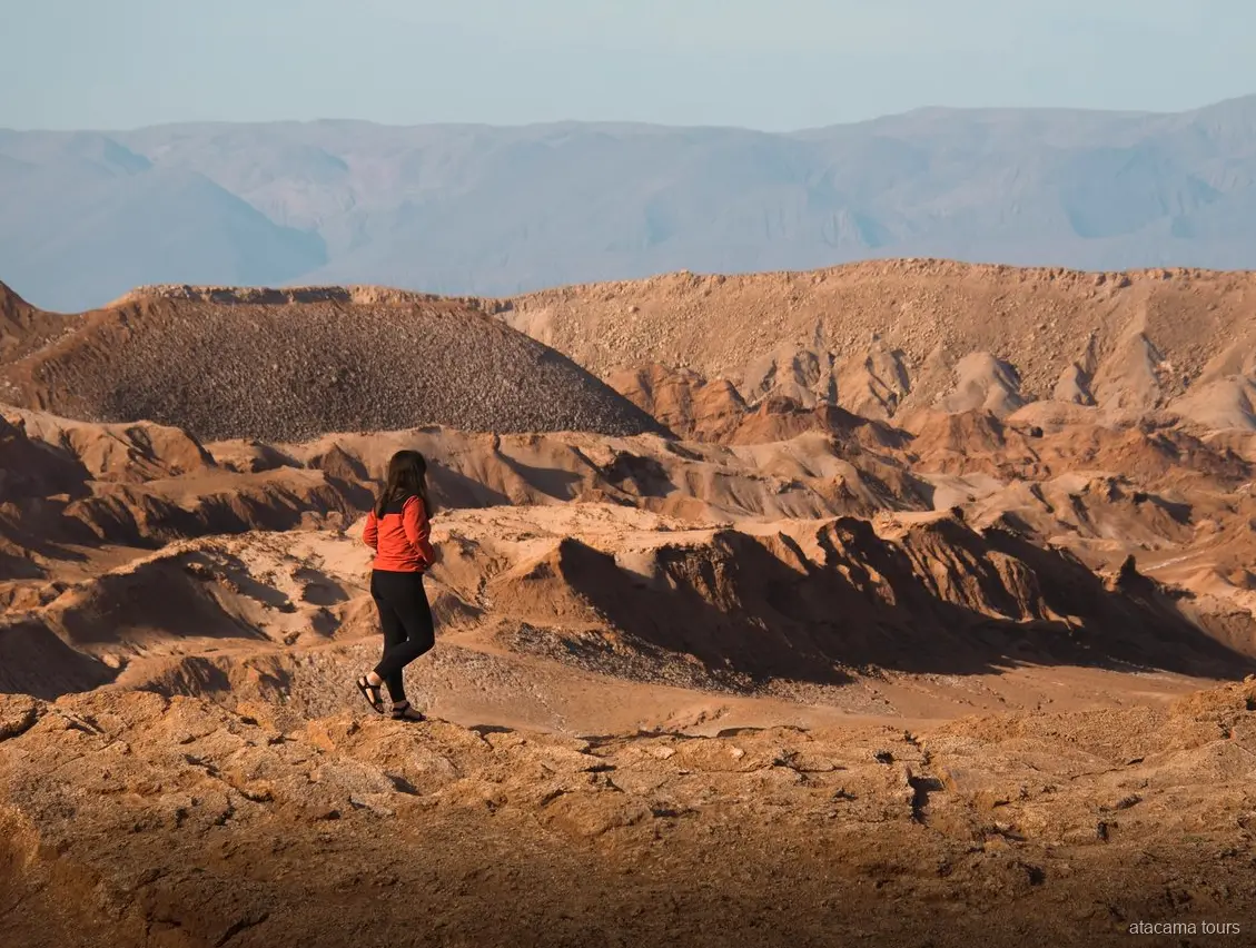 Tours en Atacama a Baltinache, caminante de chaqueta roja frente a crestas erosionadas del desierto