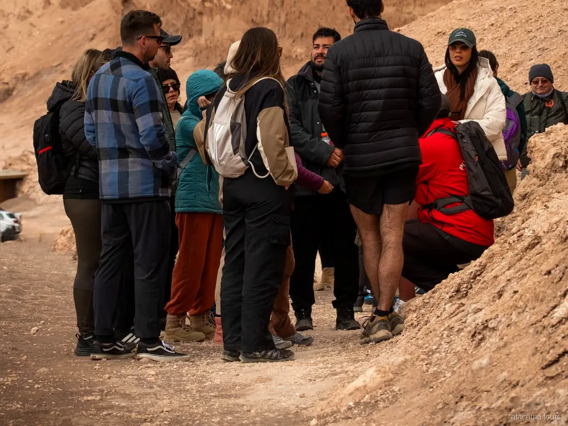 Gruppo di un tour nel deserto di Atacama con giacche pesanti riunito attorno alla guida su un sentiero del Valle de la Luna