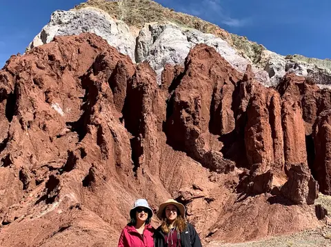 Tours en Atacama al Valle del Arcoíris, dos visitantes con sombrero ante agujas de roca roja coronadas de blanco