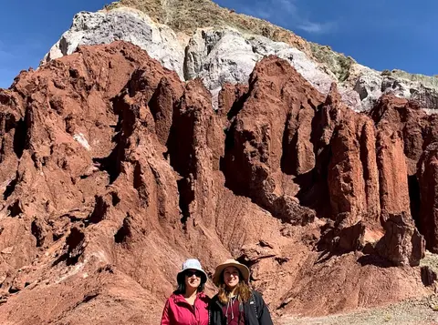Atacama tours in de Valle del Arcoiris, twee bezoekers met hoed voor grillige rode rotspieken met witte top